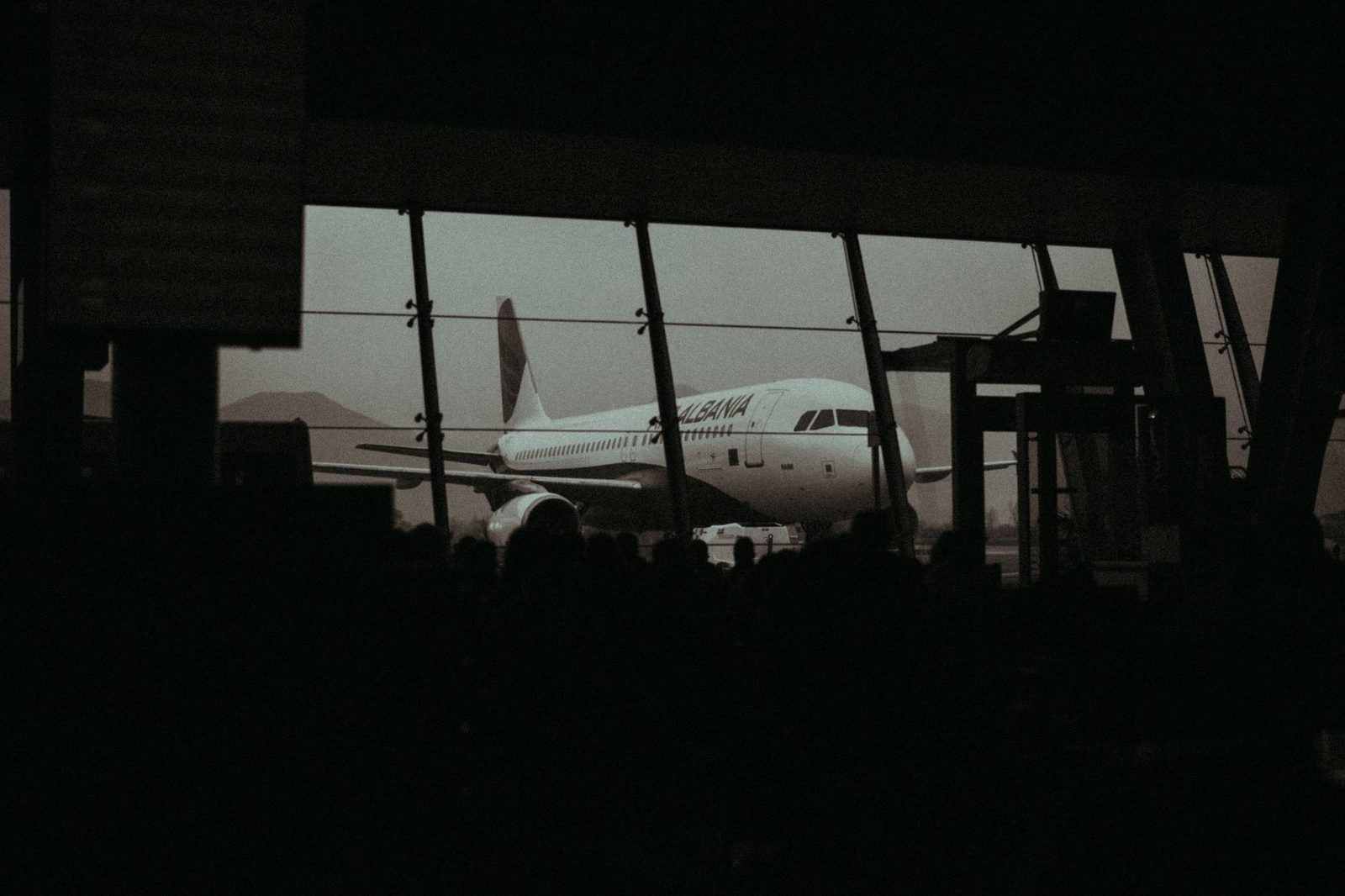 Silhouette of an airplane and waiting passengers inside an airport terminal at dusk.