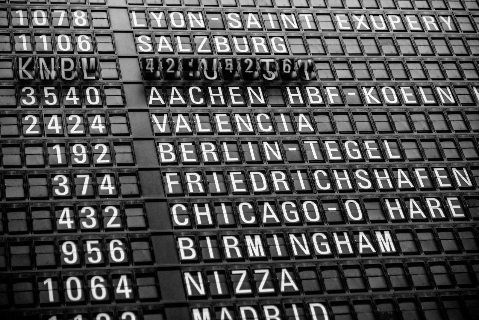 Black and white image of a vintage airport departure board displaying various international destinations.