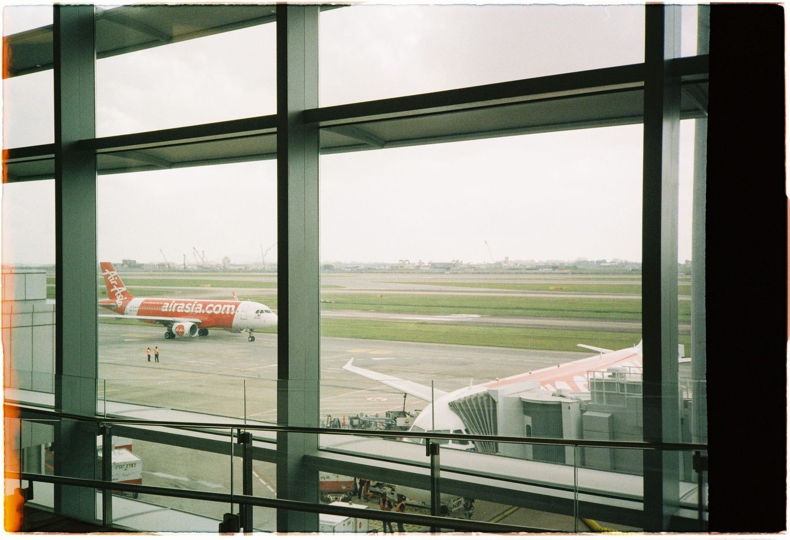 View of an AirAsia plane taxiing on the runway from inside the airport terminal.