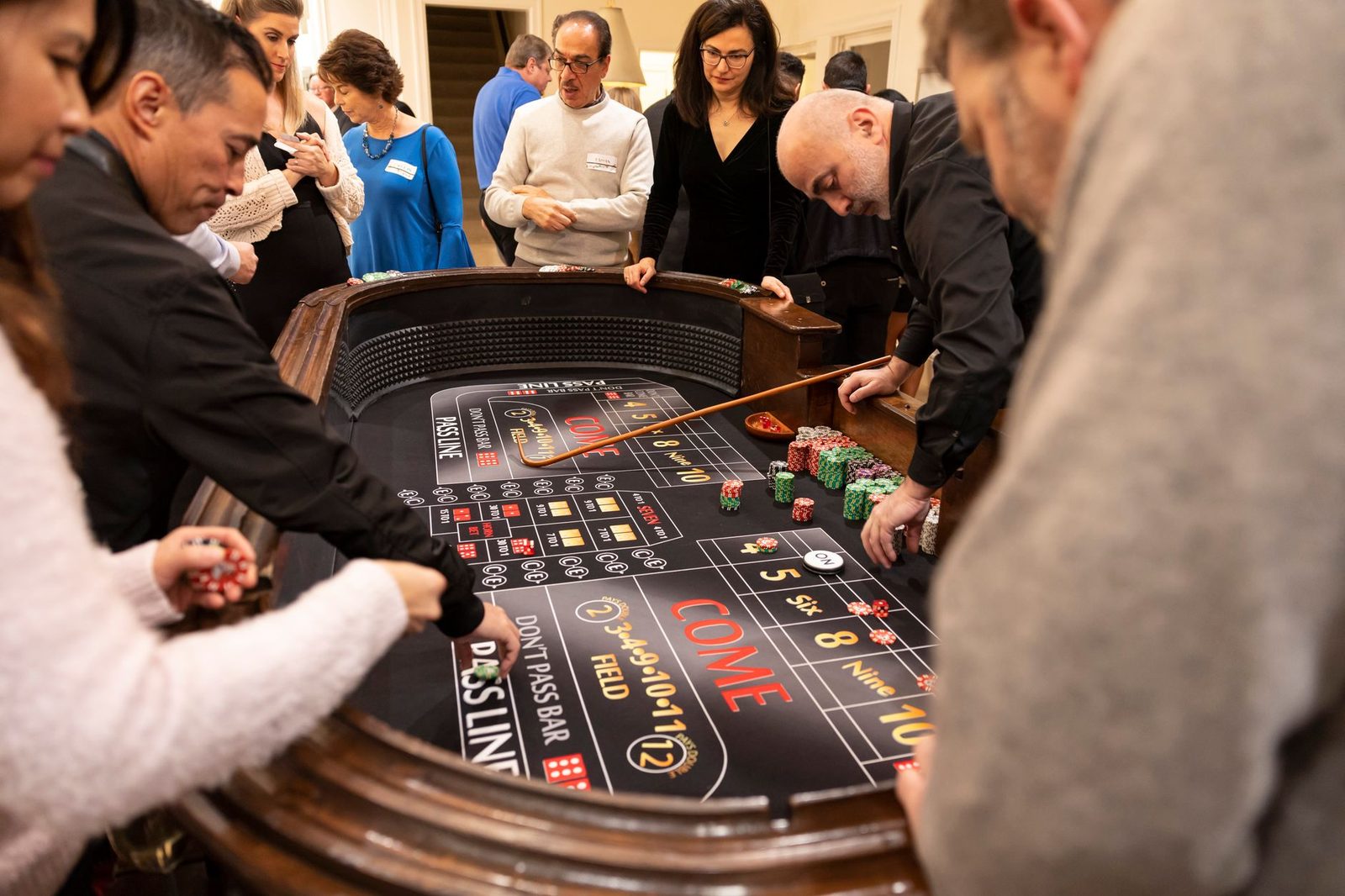 Group of adults playing craps around a casino table, engaging in betting and socializing.