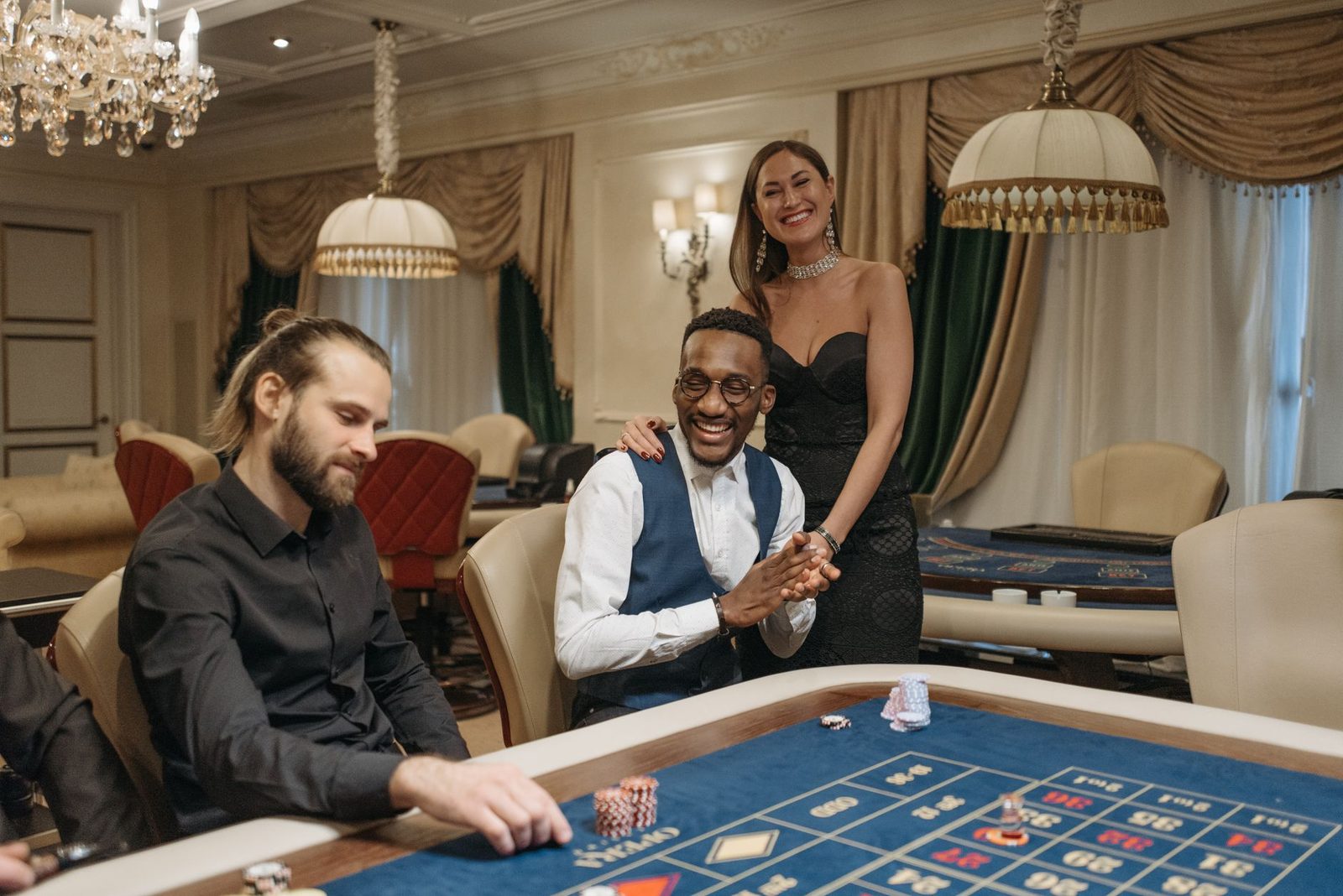 Three people enjoying a night at an elegant casino gambling table.