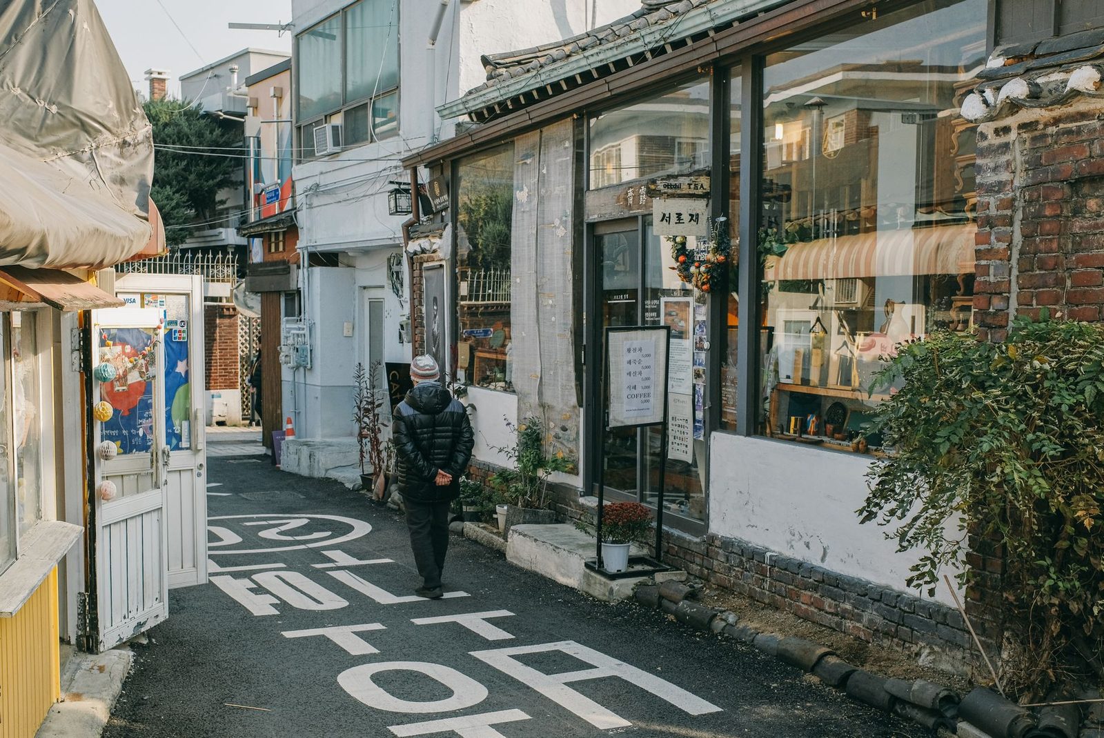 A pedestrian strolls down a quaint alley lined with shops in Seoul, capturing urban charm.