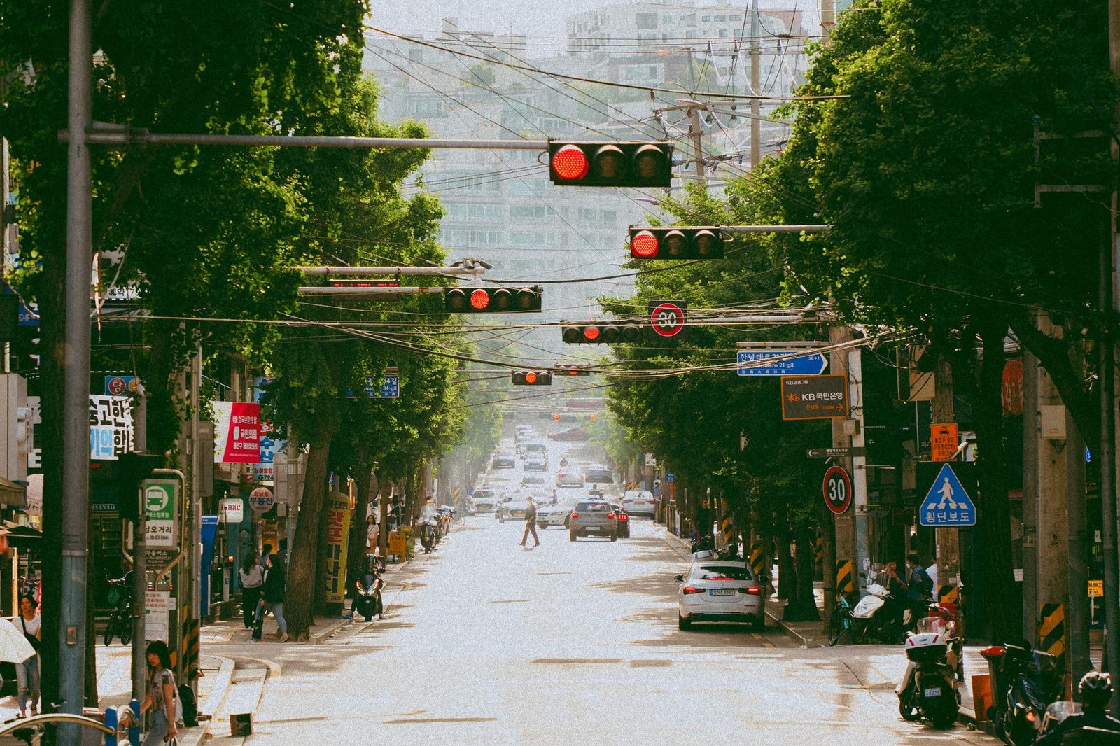 Vibrant city street with traffic lights and pedestrians under summer sunlight.