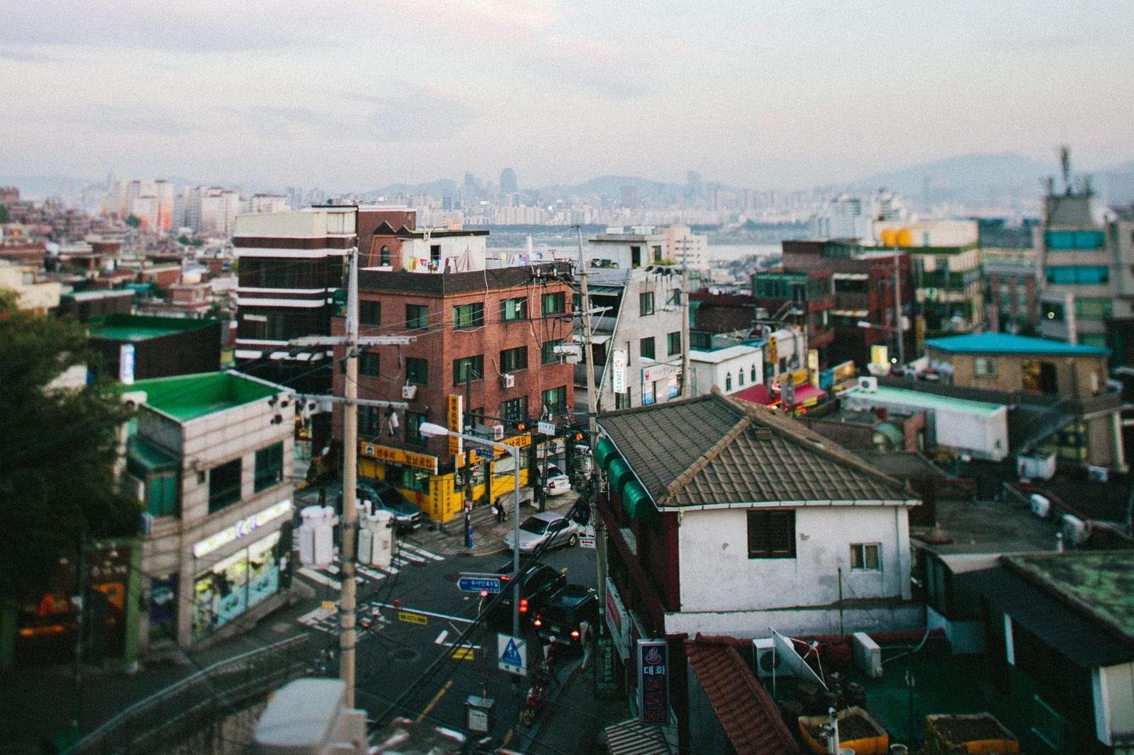 A bustling urban neighborhood with a view of the distant Seoul skyline, captured from above.