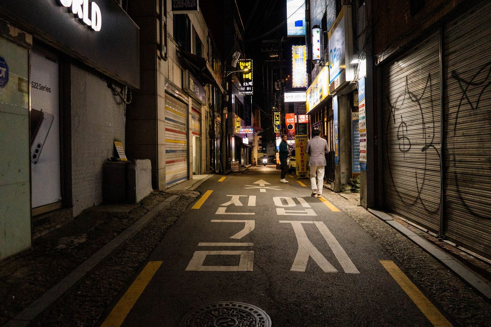 Nighttime urban scene in a narrow street of Seoul, showcasing vibrant city life and architecture.