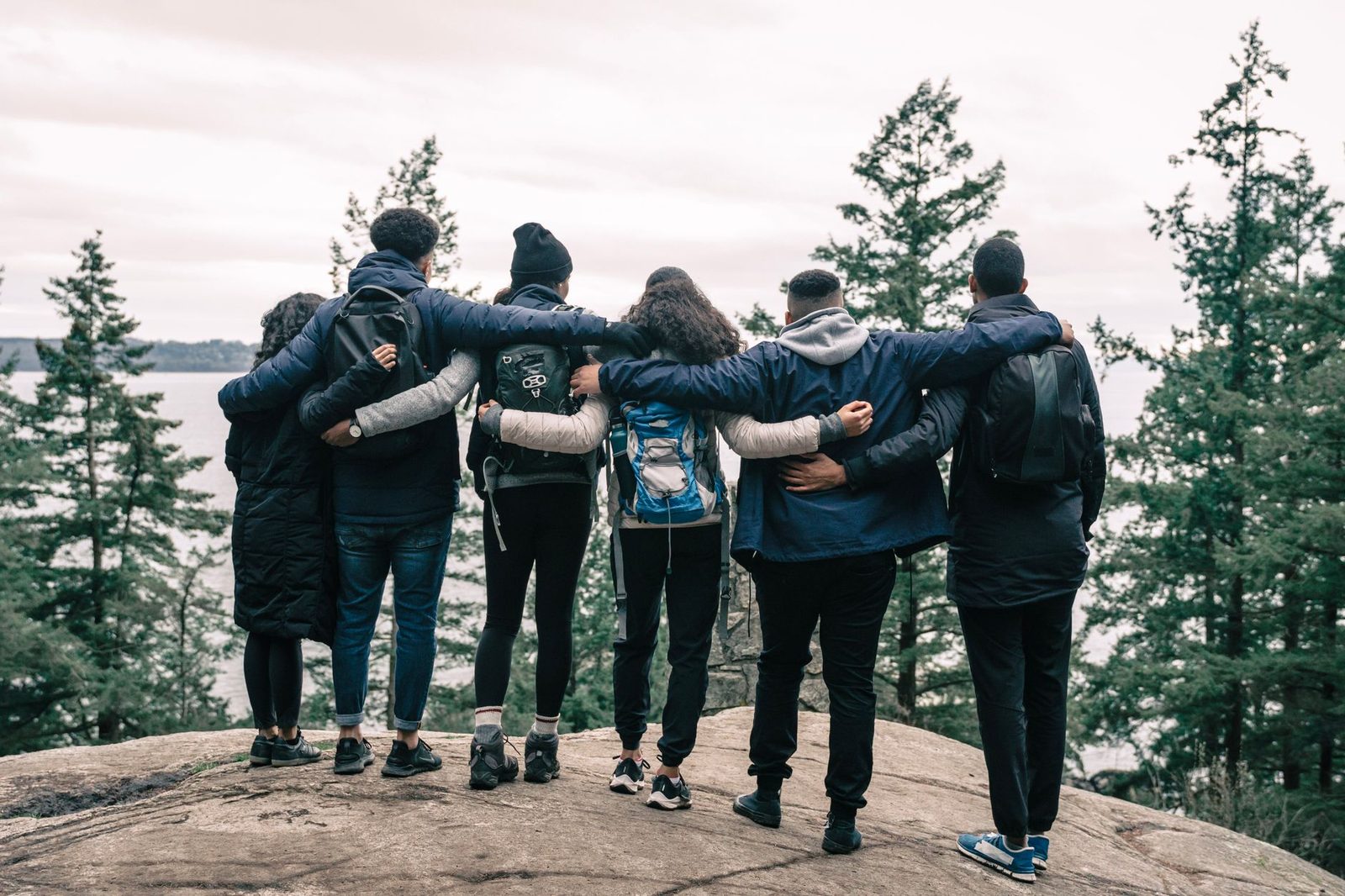 Back view of friends embracing on a scenic cliff, enjoying nature and friendship.