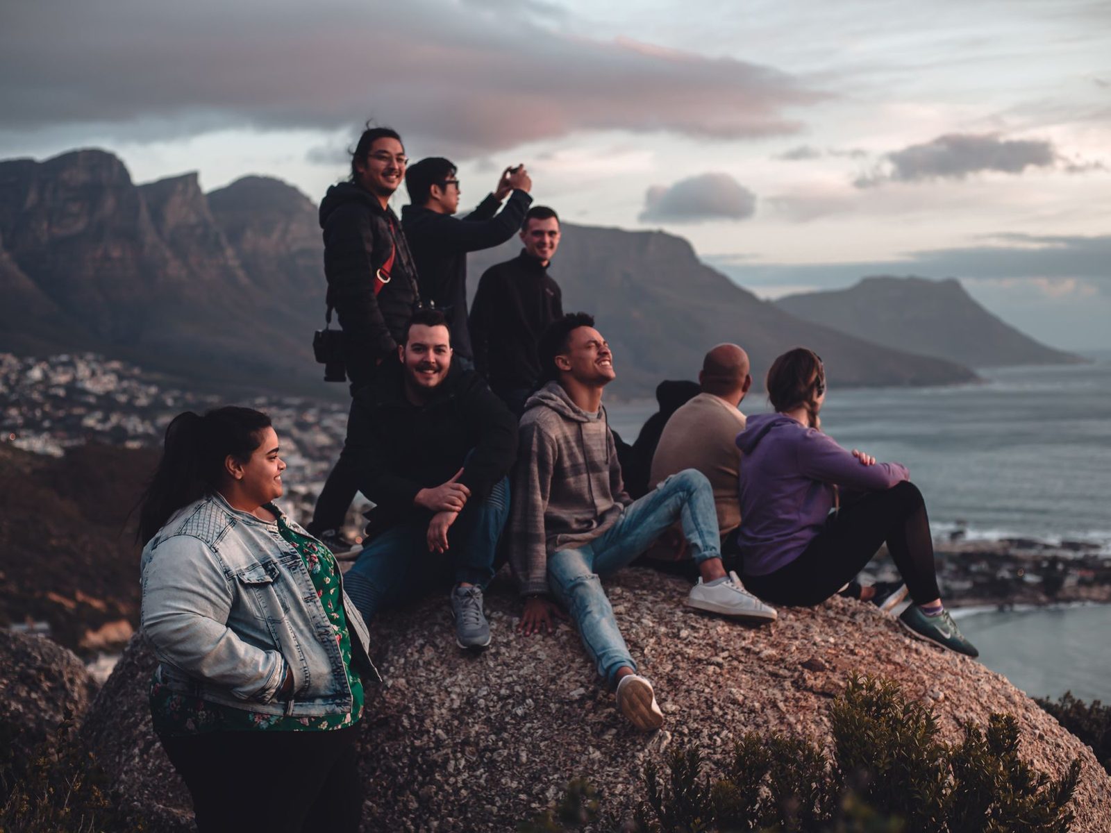 A diverse group of friends sitting on a rock, enjoying a scenic mountain view at sunset.