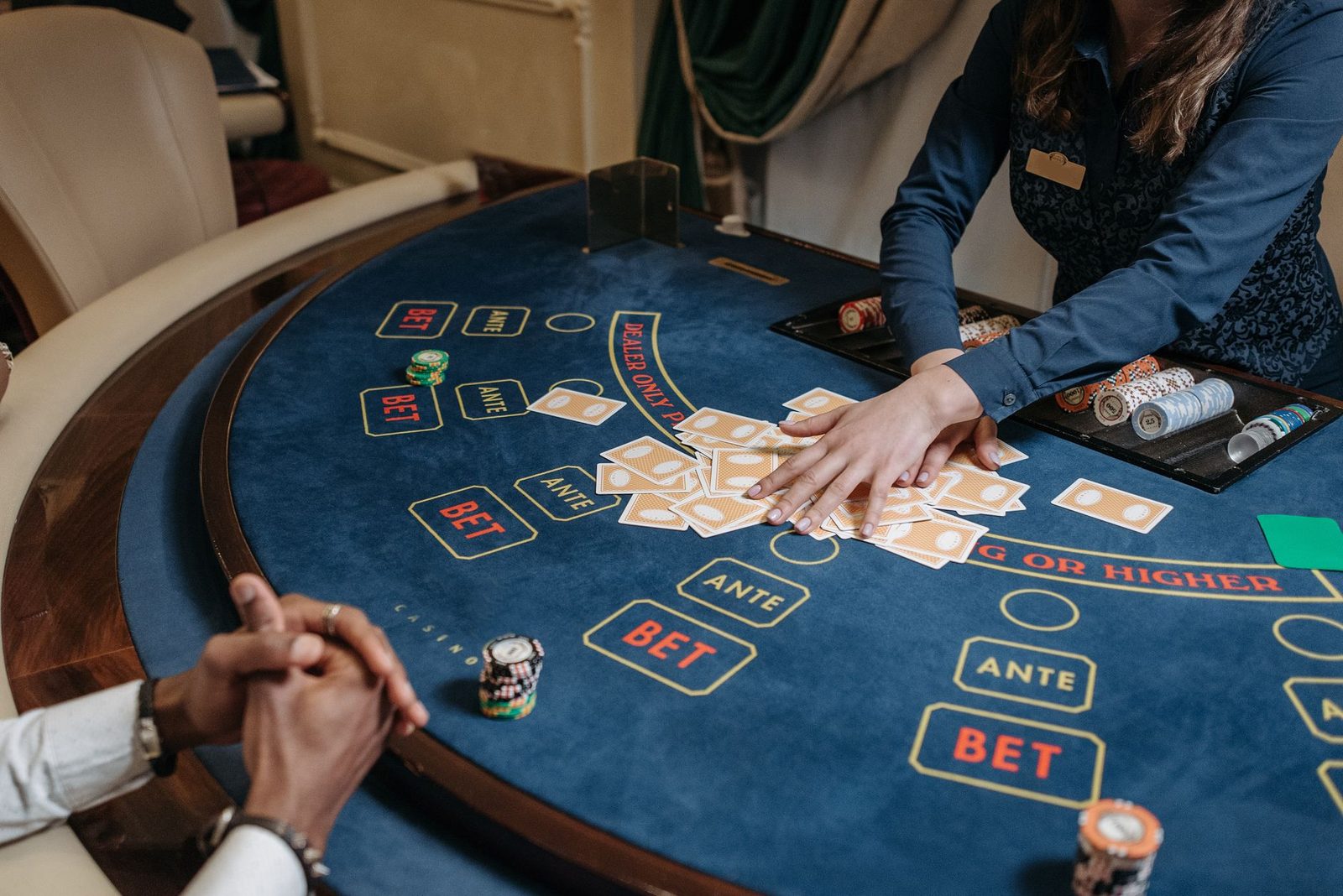 Close-up of a casino dealer shuffling cards on a gambling table with chips and bet labels.