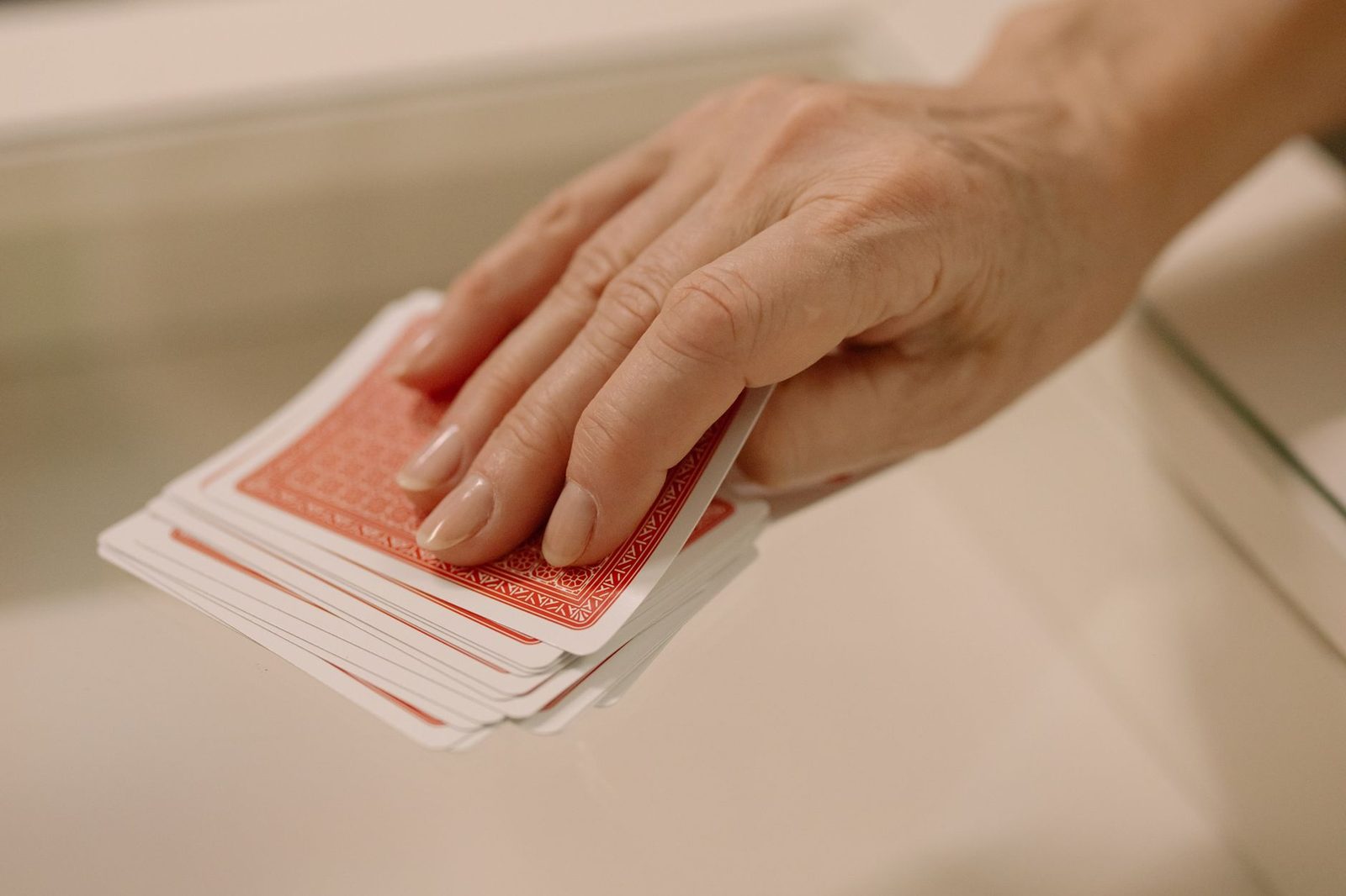 Hand selecting cards from deck on glass table reflects playful and recreational theme.