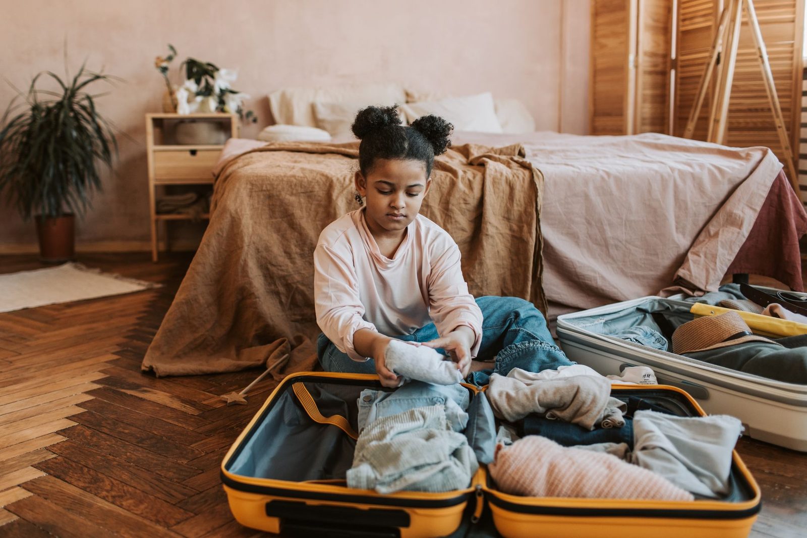 A young girl folding clothes into a suitcase in a cozy bedroom setting with natural decor.