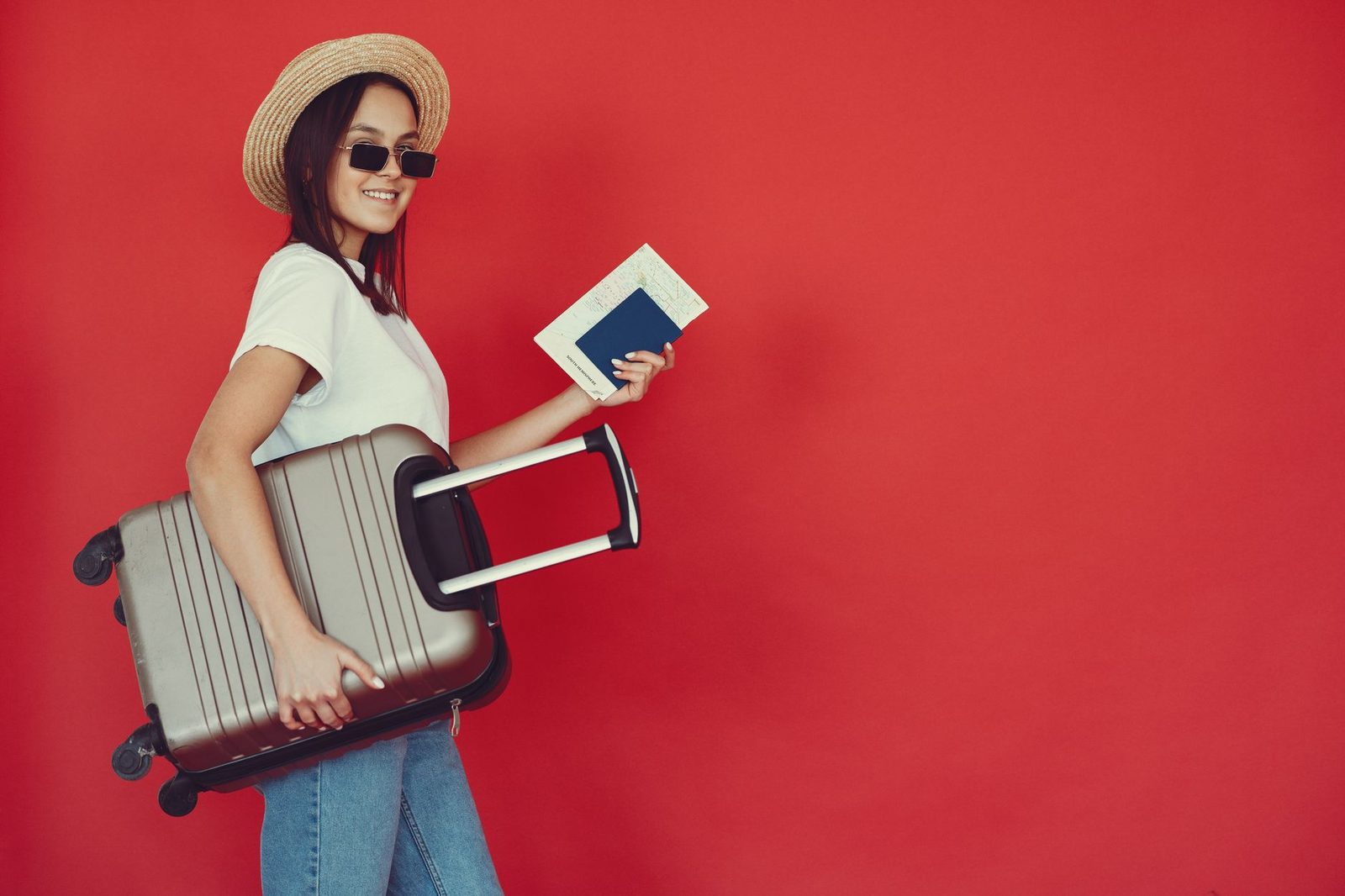 Side view of cheerful young woman with passport and tickets smiling and looking at camera while walking with baggage on