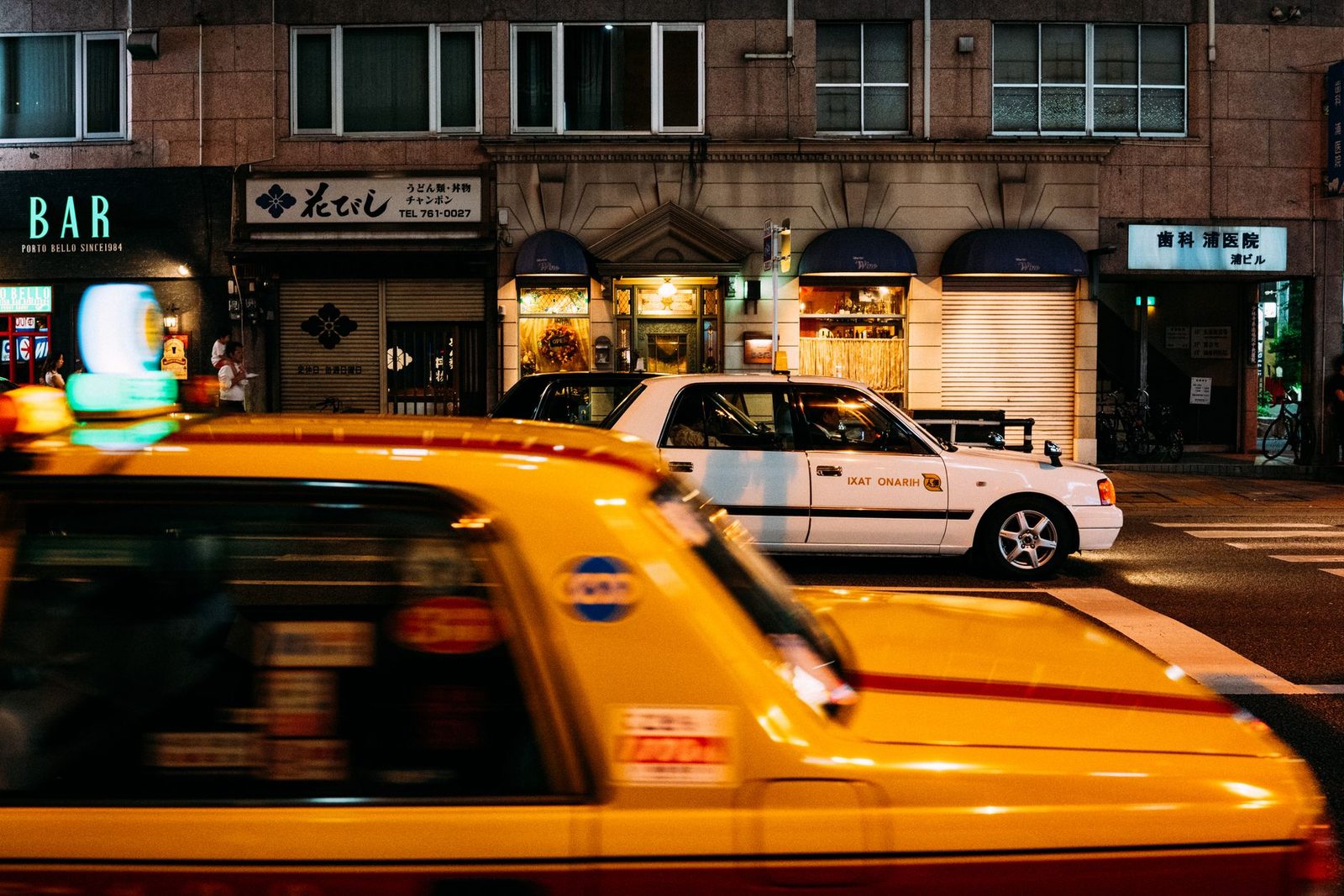 Dynamic Tokyo street scene featuring yellow taxis and illuminated storefronts at night.